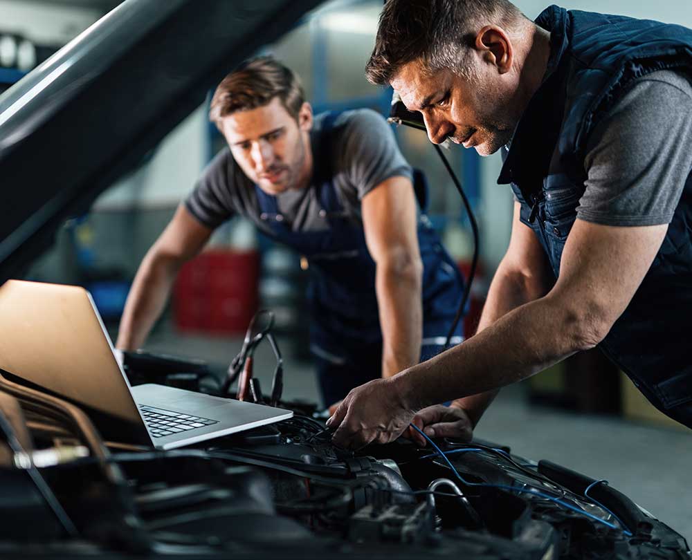 Two technicians reading live data from a scan tool and a laptop over an open engine bay