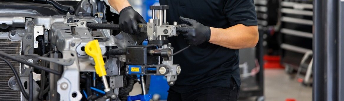 Gloved hands setting a measuring gauge against a car's radiator support