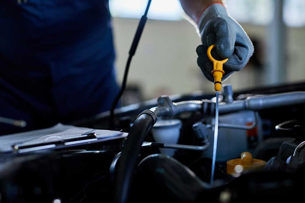 A gloved hand drawing the oil dipstick from an engine