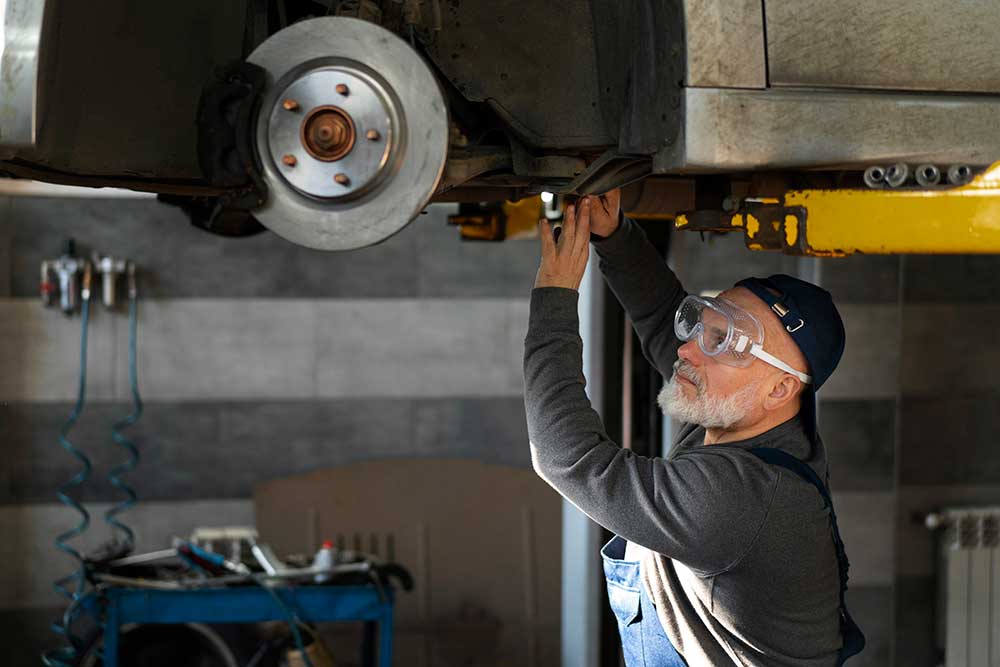 A technician on a lift inspecting the underside of a car at the front hub
