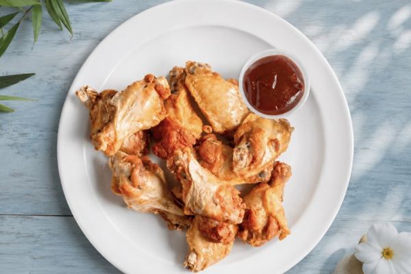 A plate of golden chicken wings with a cup of dipping sauce.