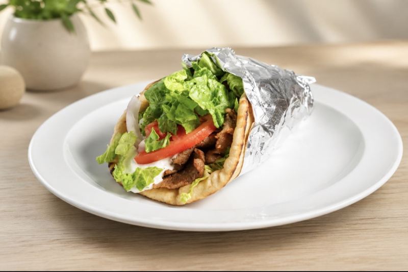 A gyro wrapped in warm pita with lettuce, tomato and white sauce.