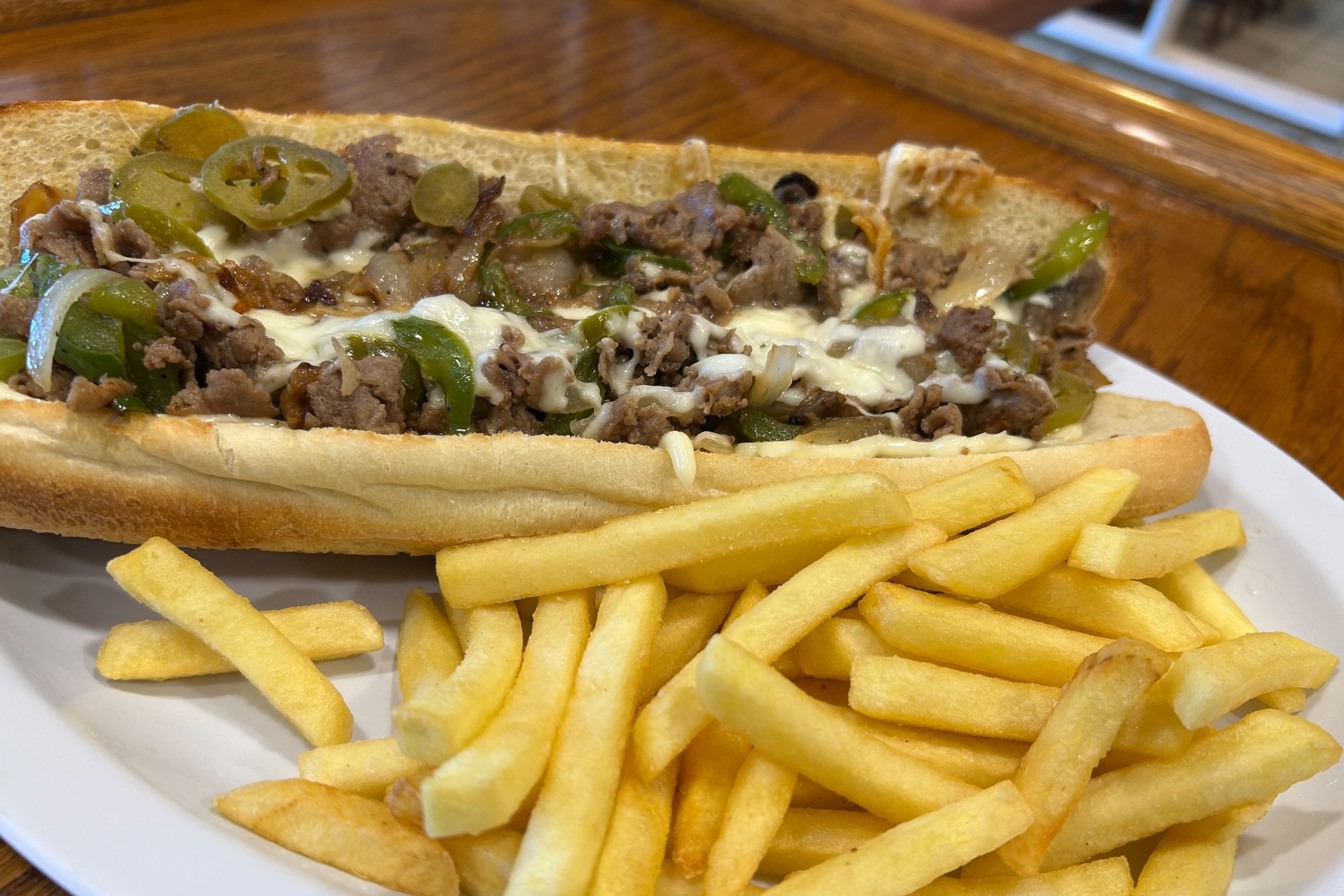 A Philly cheesesteak loaded with peppers and melted cheese, served with fries.