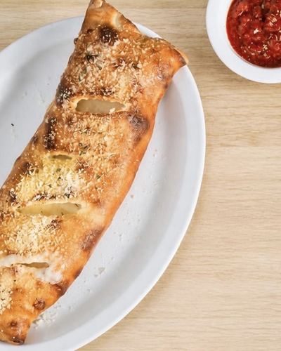A long stromboli, vented along the top and dusted with parmesan, with a cup of marinara alongside.