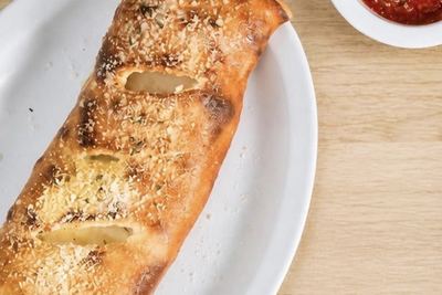 A long stromboli, vented along the top and dusted with parmesan, with a cup of marinara alongside.