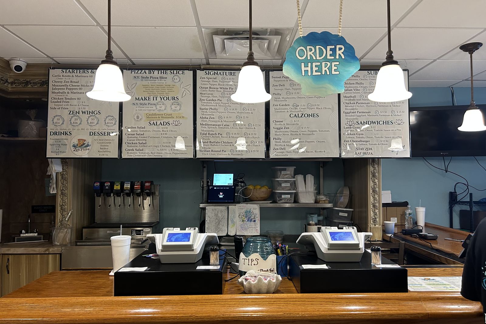 The order counter under the hand-lettered menu boards, with the painted ORDER HERE sign hanging above it.
