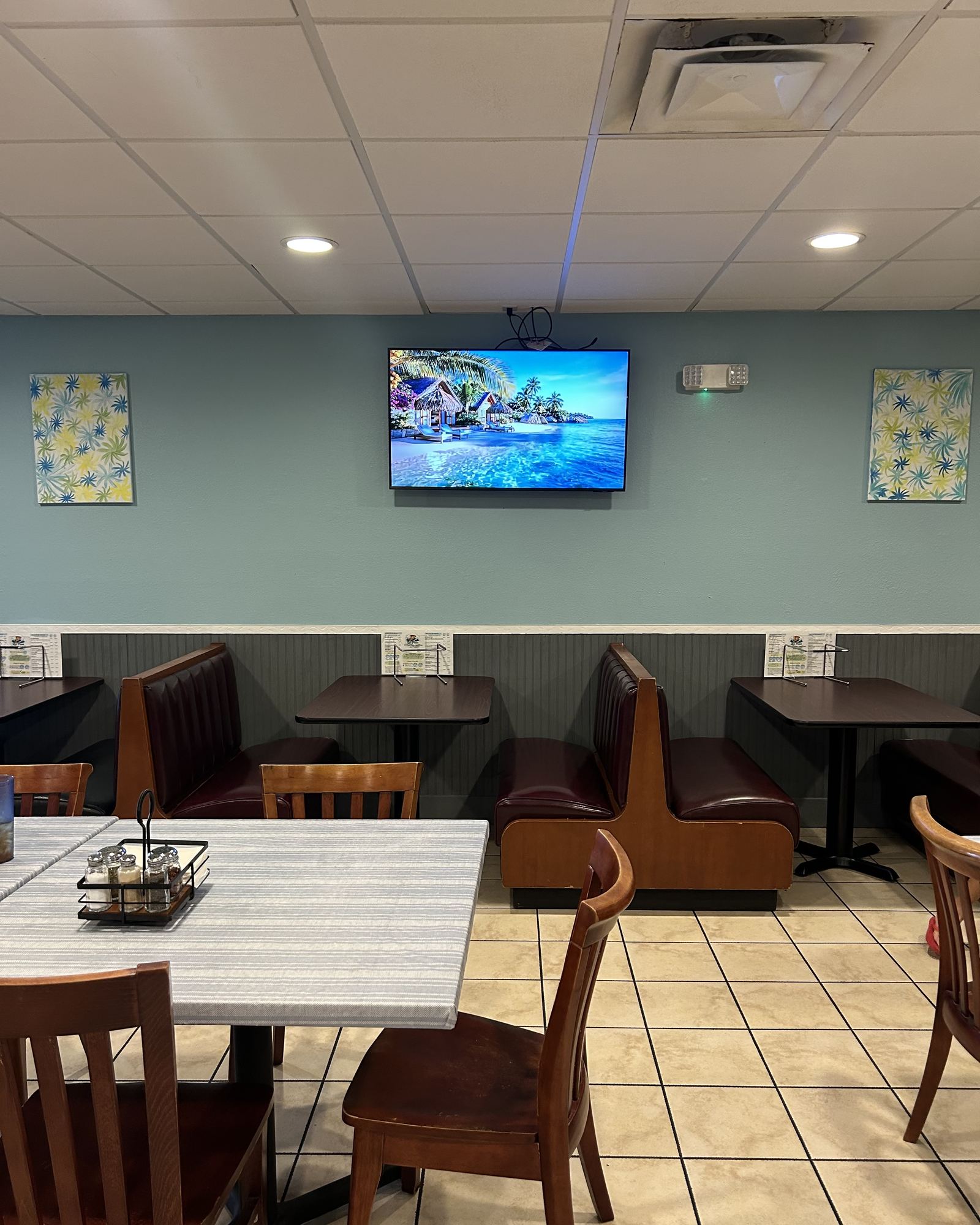 The dining room: leather booths along a sea-green wall, tables laid with salt and pepper, and a beach scene on the television.
