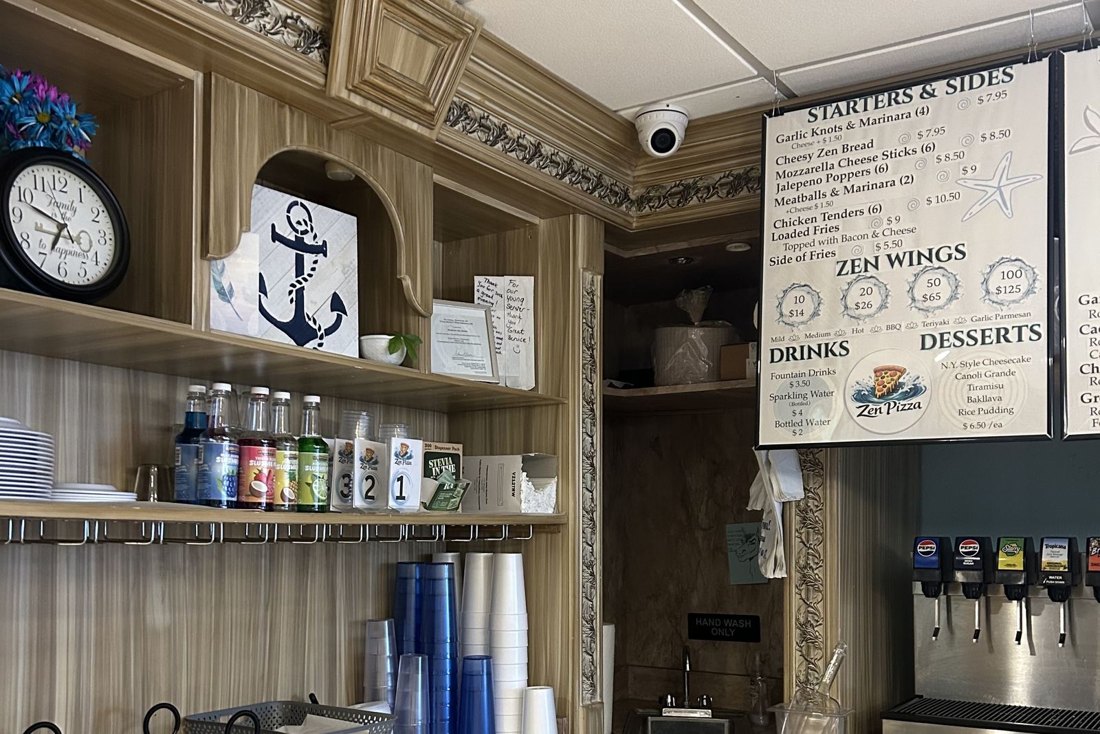 The drinks station: a soda fountain, stacked cups and bottled drinks on the shelf, under the menu board.