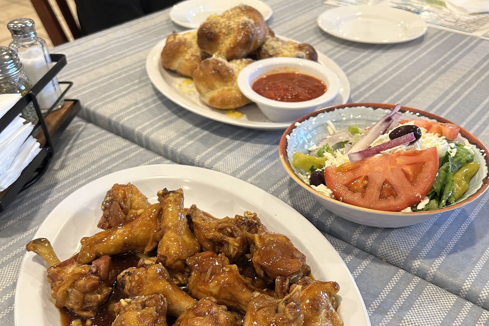 A table in the dining room: a platter of glazed wings, garlic knots with a cup of marinara, and a Greek salad.